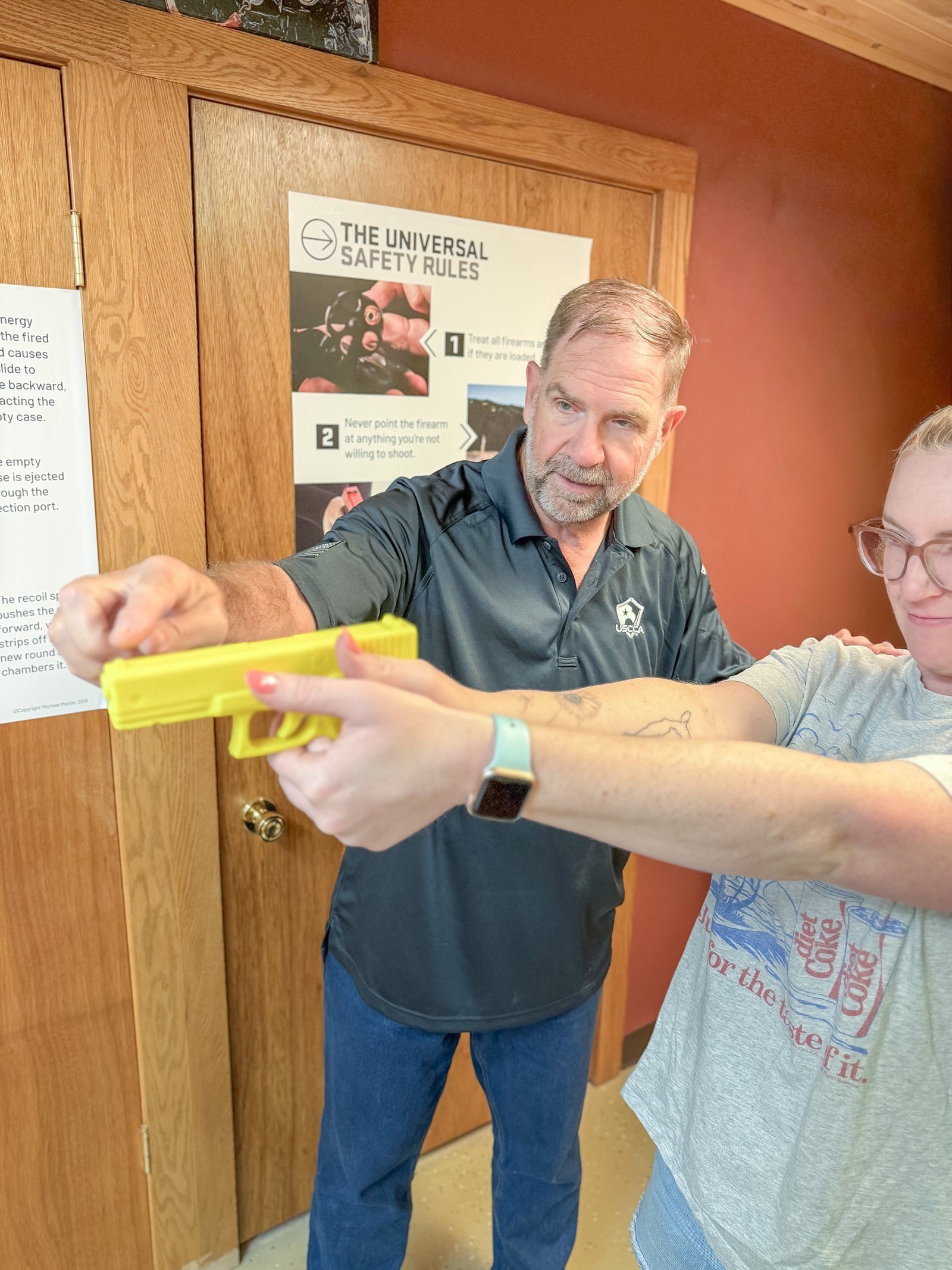 Michael Cannon coaching a student's grip and aim with a bright yellow inert training pistol