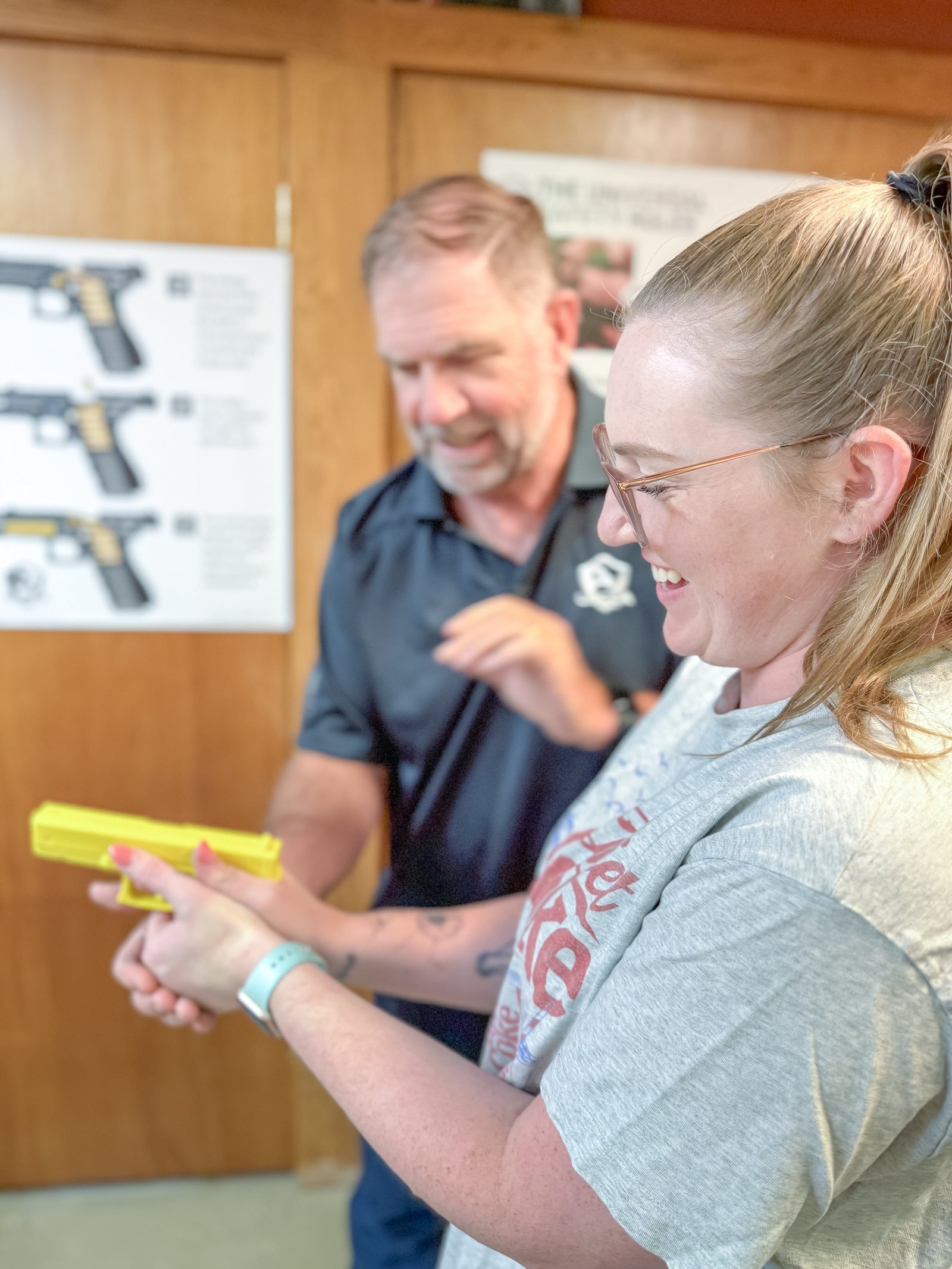A student smiling while practicing with a bright yellow inert training pistol as Michael coaches nearby